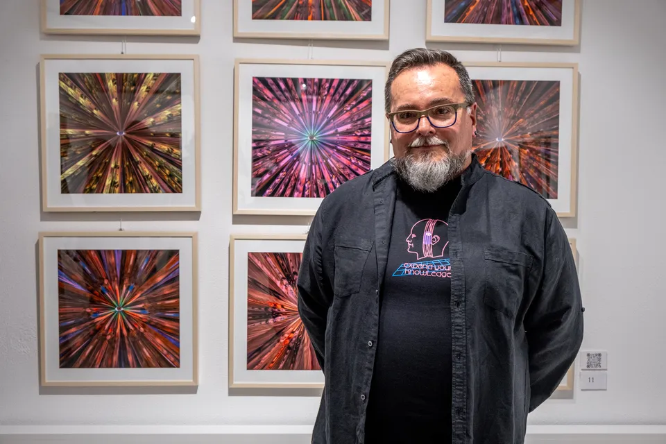 O artista diante de uma parede com impressões quadradas de G.O.D. emolduradas, na Bull & Stein Gallery.